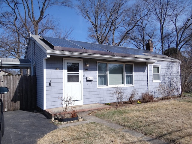 ranch-style home featuring roof mounted solar panels, a chimney, a front yard, and fence