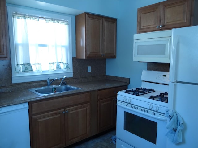 kitchen featuring tasteful backsplash, white appliances, dark countertops, and a sink