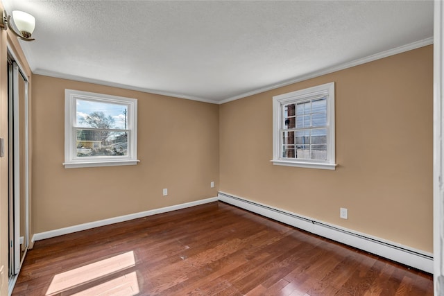 spare room featuring baseboards, baseboard heating, wood finished floors, and ornamental molding