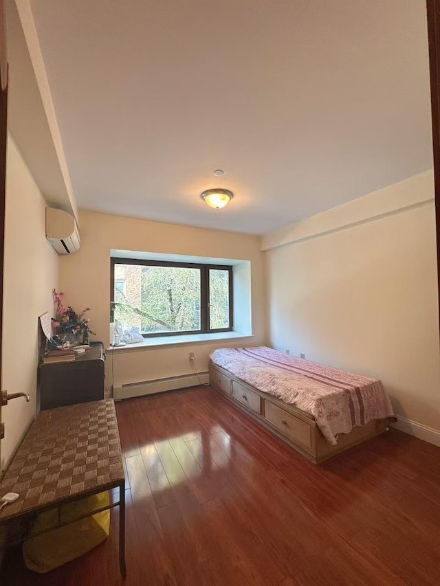 bedroom featuring a baseboard radiator, baseboards, an AC wall unit, and wood finished floors