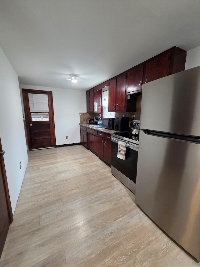 kitchen featuring light wood finished floors, appliances with stainless steel finishes, baseboards, and a sink