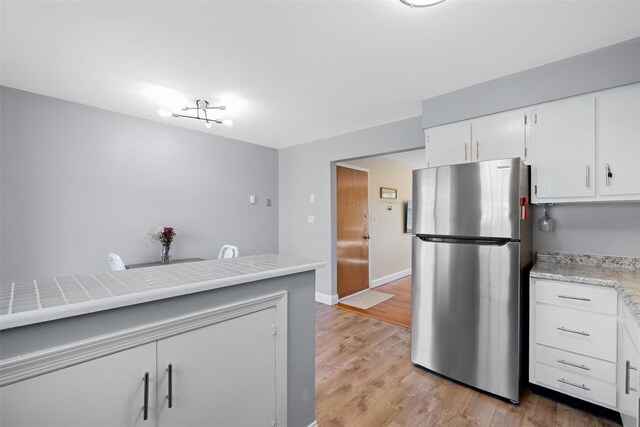 kitchen featuring baseboards, light countertops, freestanding refrigerator, light wood-style floors, and white cabinets