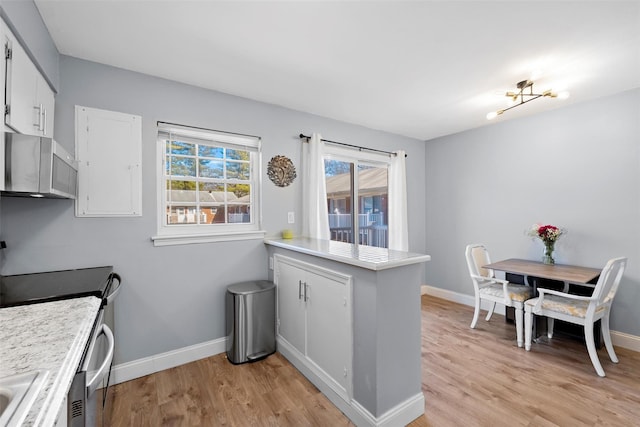 kitchen with stainless steel microwave, a peninsula, light wood-style flooring, and light countertops