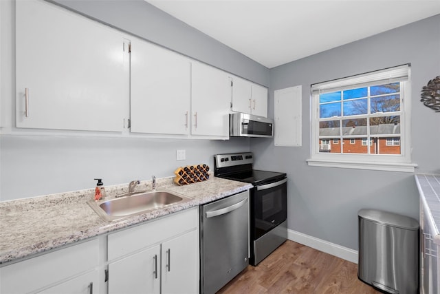 kitchen featuring baseboards, appliances with stainless steel finishes, wood finished floors, white cabinetry, and a sink