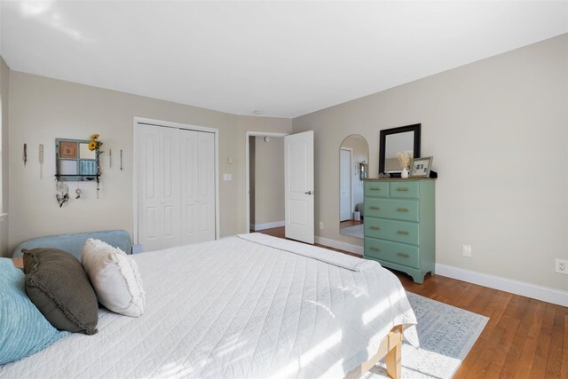 bedroom featuring arched walkways, baseboards, a closet, and wood finished floors