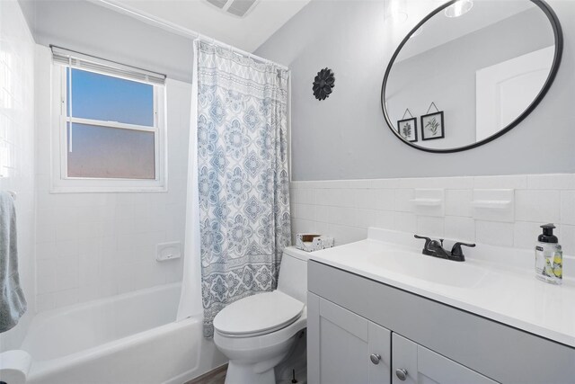 bathroom with visible vents, toilet, vanity, shower / bath combination with curtain, and tile walls