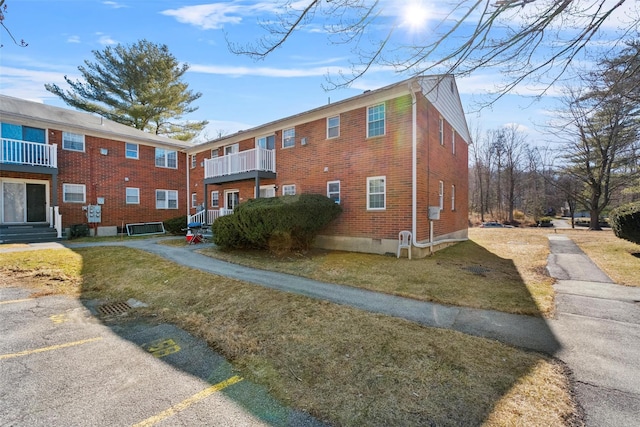 view of side of property featuring brick siding, uncovered parking, a balcony, and entry steps