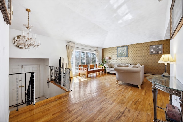 living room featuring a notable chandelier, wood finished floors, stairway, wallpapered walls, and vaulted ceiling