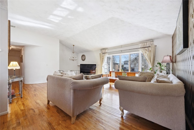 living area featuring a notable chandelier, light wood-style flooring, and lofted ceiling