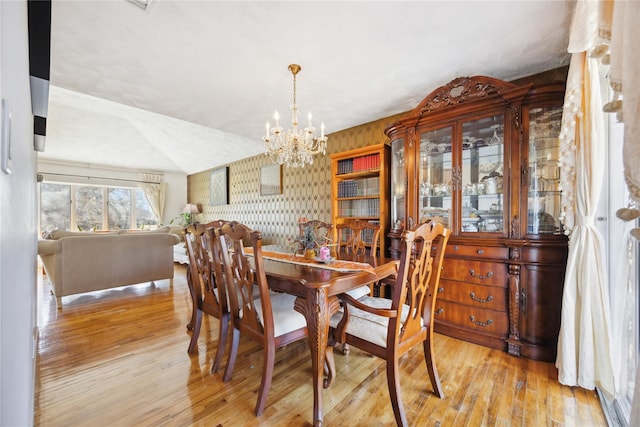 dining area featuring an inviting chandelier, wallpapered walls, lofted ceiling, and hardwood / wood-style flooring