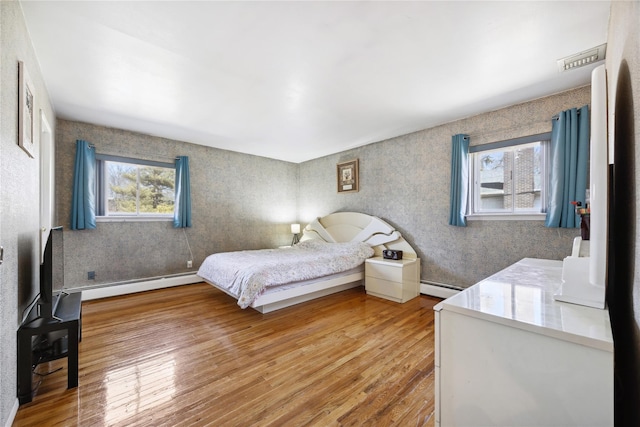 bedroom with a baseboard heating unit, light wood-style floors, and visible vents