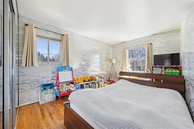 bedroom with multiple windows, wallpapered walls, and wood finished floors