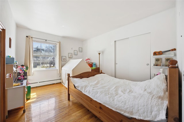 bedroom with wood finished floors, a closet, and a baseboard radiator