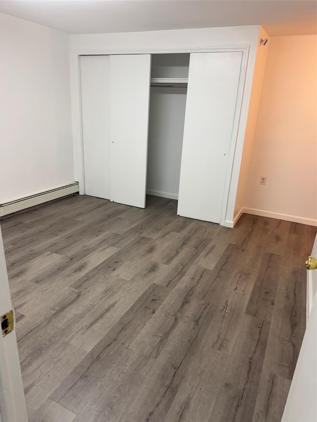 unfurnished bedroom with a closet, a baseboard heating unit, baseboards, and wood finished floors