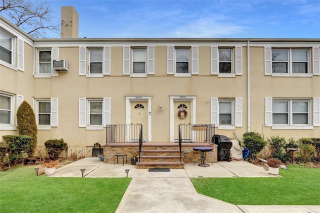 townhome / multi-family property with a chimney, stucco siding, a wall mounted air conditioner, and a front lawn