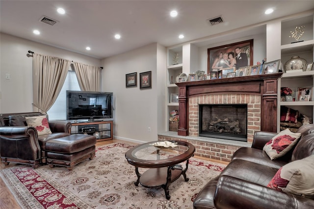 living area with a brick fireplace, wood finished floors, and visible vents