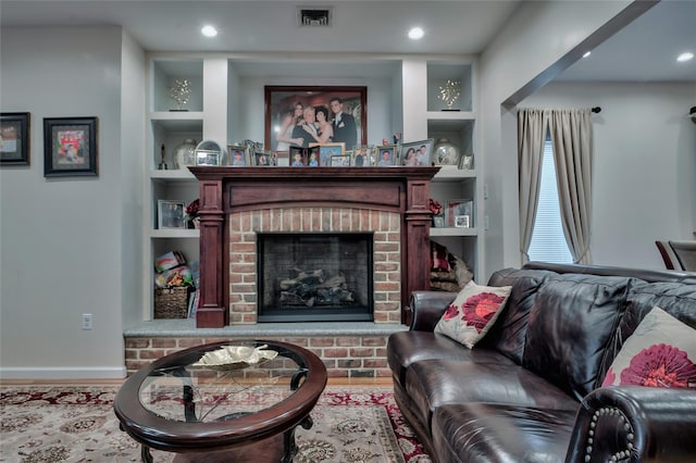 living area with visible vents, built in features, wood finished floors, a fireplace, and baseboards