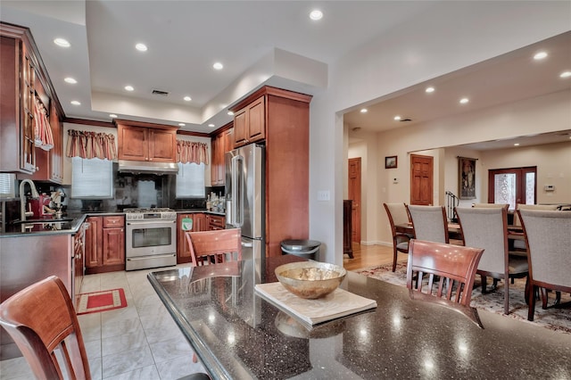 kitchen featuring visible vents, a sink, under cabinet range hood, tasteful backsplash, and appliances with stainless steel finishes