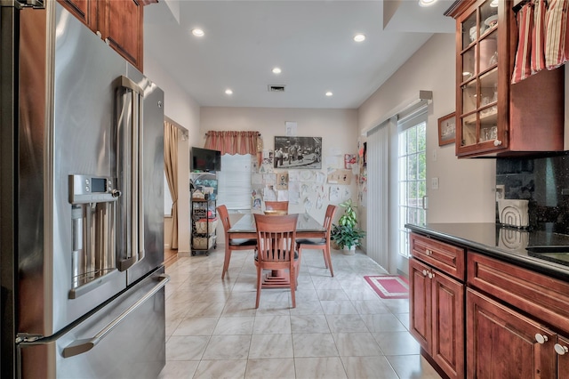 kitchen featuring visible vents, dark countertops, tasteful backsplash, high quality fridge, and glass insert cabinets