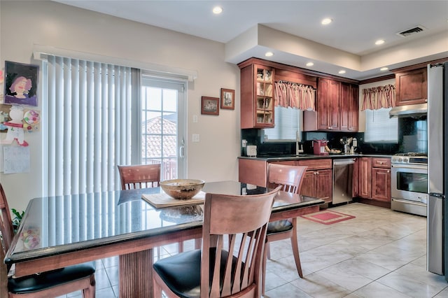 kitchen with under cabinet range hood, stainless steel appliances, tasteful backsplash, and dark countertops