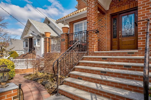 doorway to property featuring fence, brick siding, a chimney, and a tiled roof