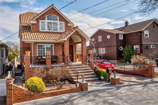 view of front of property with an AC wall unit, brick siding, a porch, and a tile roof