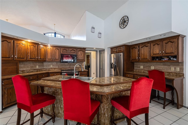 kitchen featuring a kitchen bar, vaulted ceiling, stainless steel appliances, light tile patterned flooring, and an island with sink