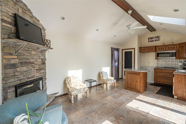 kitchen featuring stainless steel microwave, backsplash, a kitchen island, vaulted ceiling with skylight, and brown cabinetry