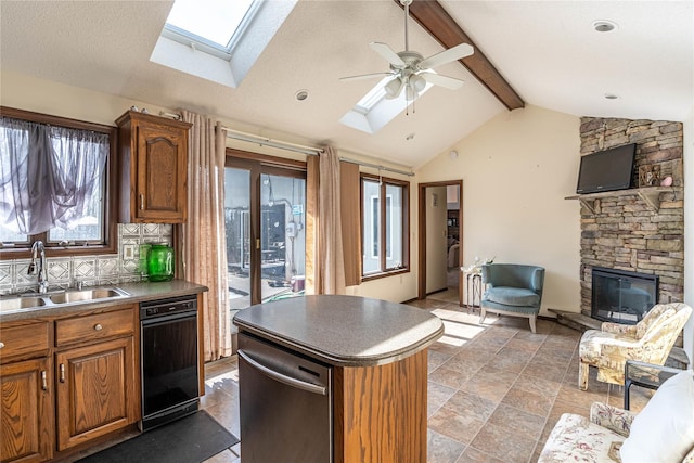kitchen featuring vaulted ceiling with skylight, a sink, a fireplace, brown cabinetry, and decorative backsplash