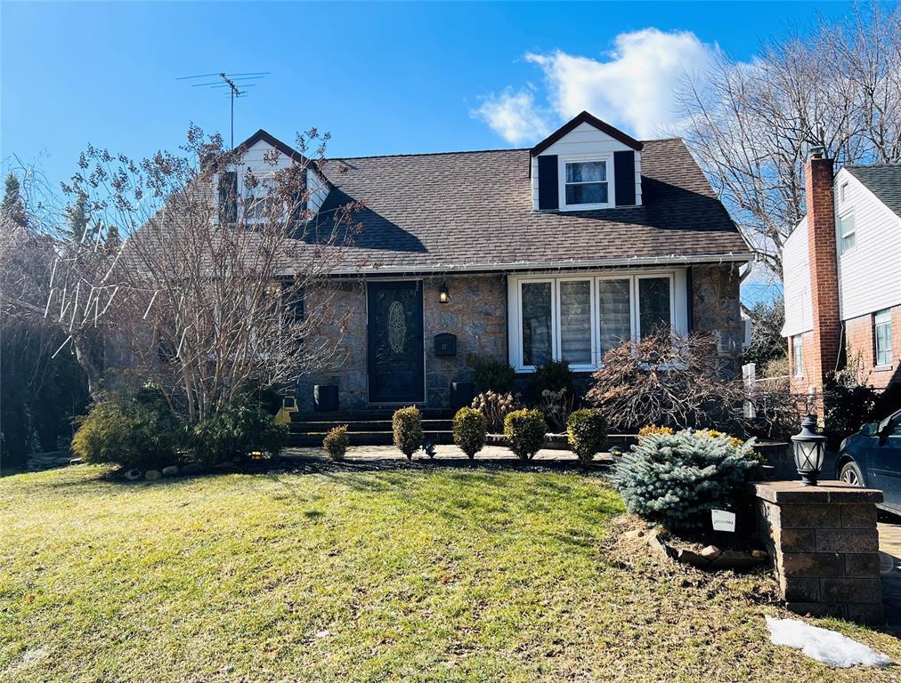 cape cod home with stone siding, a front yard, and a shingled roof