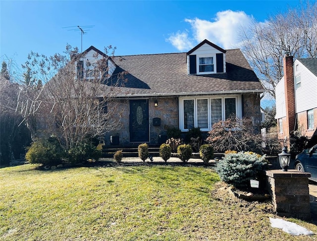 cape cod home with stone siding, a front yard, and a shingled roof