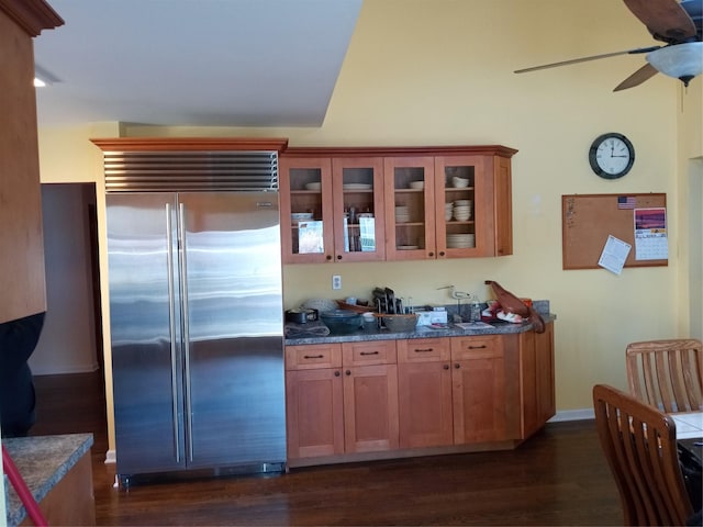 kitchen with brown cabinetry, glass insert cabinets, dark wood-style flooring, and built in fridge