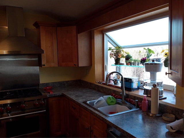 kitchen featuring dark countertops, wall chimney range hood, brown cabinetry, high end stainless steel range, and a sink