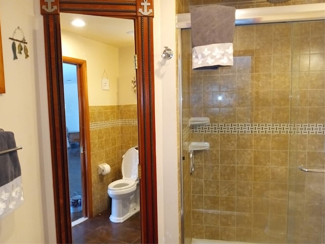 full bathroom with tile patterned flooring, toilet, wainscoting, a stall shower, and tile walls