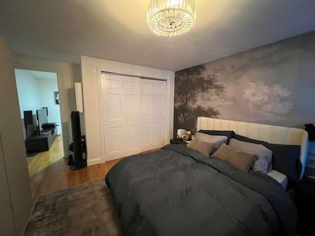 bedroom with wallpapered walls, wood finished floors, a closet, and a chandelier