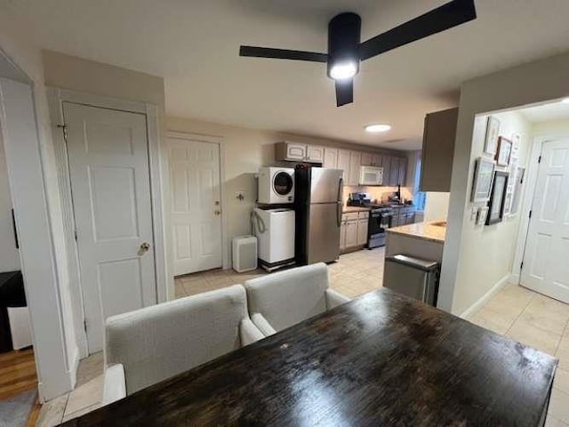 kitchen featuring stacked washer / dryer, ceiling fan, light countertops, light tile patterned flooring, and stainless steel appliances