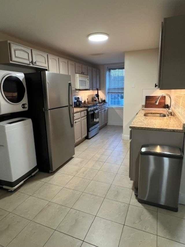 kitchen with a sink, freestanding refrigerator, range with gas cooktop, stacked washer / dryer, and white microwave