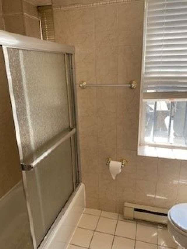 bathroom with tile patterned flooring, toilet, baseboard heating, enclosed tub / shower combo, and tile walls