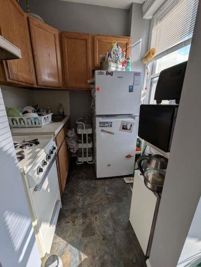 kitchen with premium range hood, white appliances, brown cabinets, and light countertops