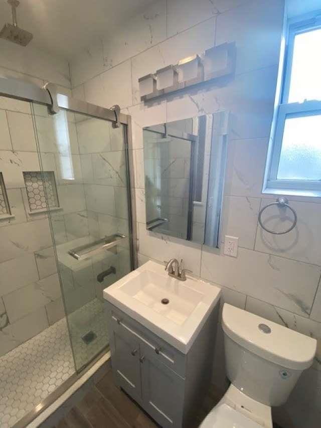 full bath with vanity, tile walls, toilet, and a stall shower