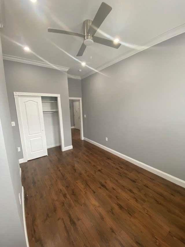 unfurnished bedroom with dark wood-type flooring, ornamental molding, a ceiling fan, a closet, and baseboards