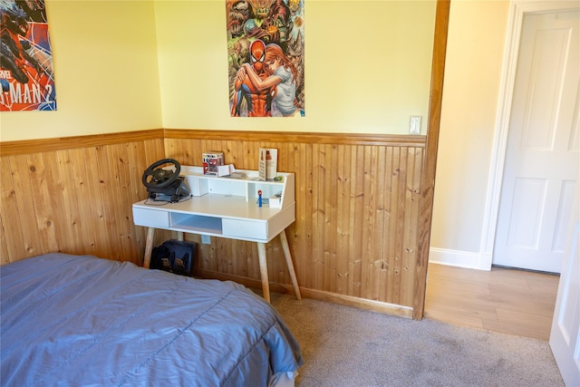 carpeted bedroom with a wainscoted wall and wooden walls