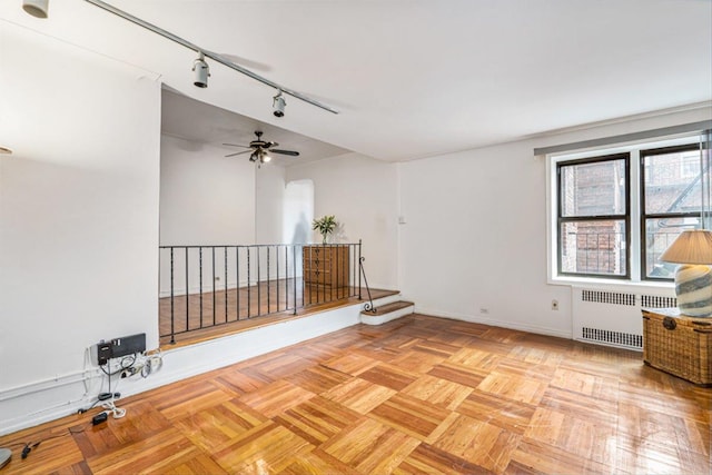 spare room featuring track lighting, radiator, a ceiling fan, and baseboards