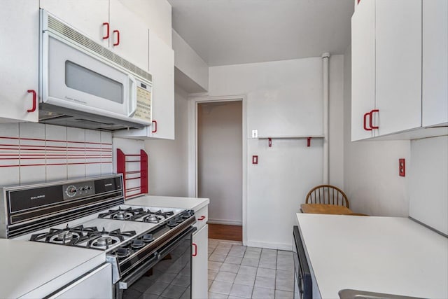 kitchen with white microwave, light countertops, decorative backsplash, gas stove, and white cabinetry