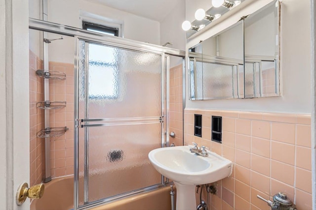 full bath featuring tile walls, shower / bath combination with glass door, and a sink