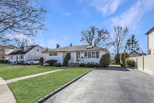 view of front of home with driveway, a chimney, a front lawn, and fence