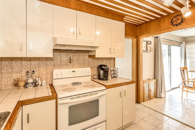 kitchen with under cabinet range hood, tile countertops, light tile patterned floors, white range with electric stovetop, and white cabinetry