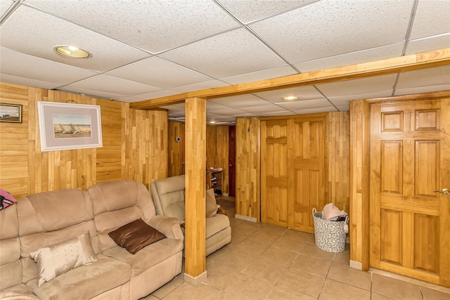 living room with light tile patterned floors, a paneled ceiling, and wood walls