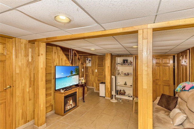 living area with light tile patterned floors, a paneled ceiling, wooden walls, and a glass covered fireplace