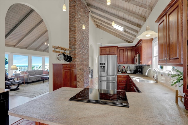 kitchen featuring cooktop, light countertops, stainless steel refrigerator with ice dispenser, arched walkways, and a sink